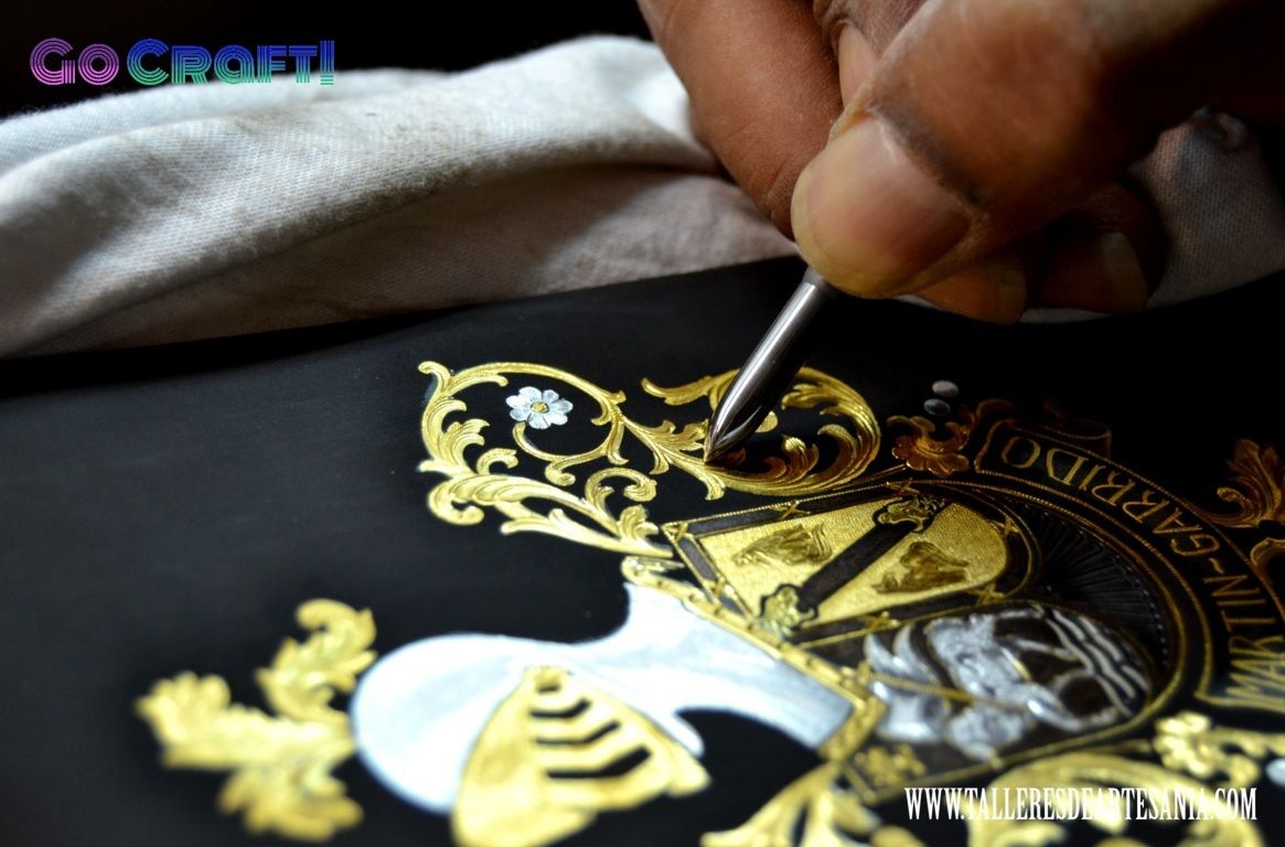 Imagen en primer plano del artesano damasquinando a mano un escudo heráldico en oro de 24 ct